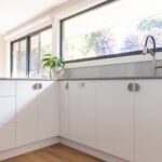 White glass splashback with white cabinetry and stone benchtops in a Canberra kitchen
