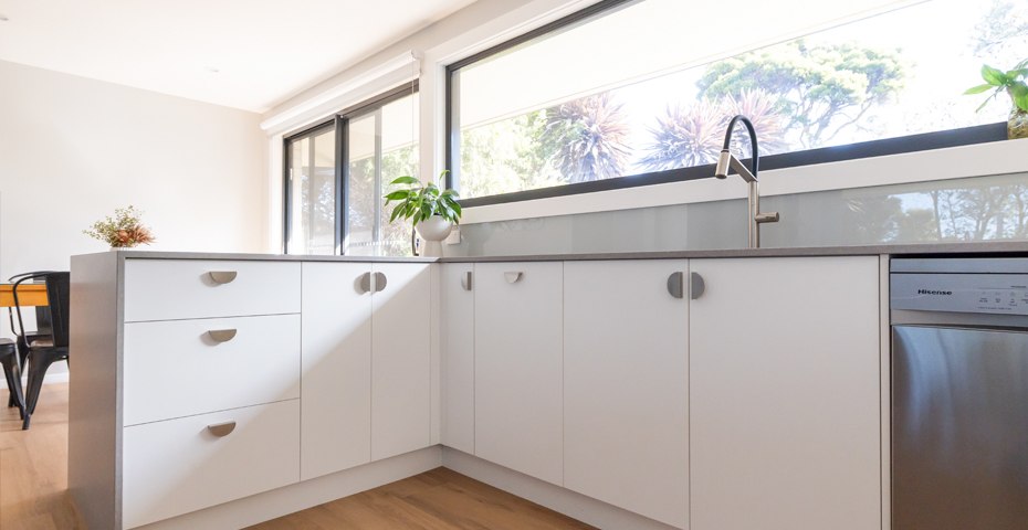 White glass splashback with white cabinetry and stone benchtops in a Canberra kitchen